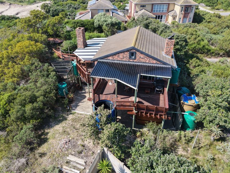 Aerial view of a detached house featuring a tiled roof, brick chimneys, extensive timber decking, and multiple water storage tanks set in a natural landscape.