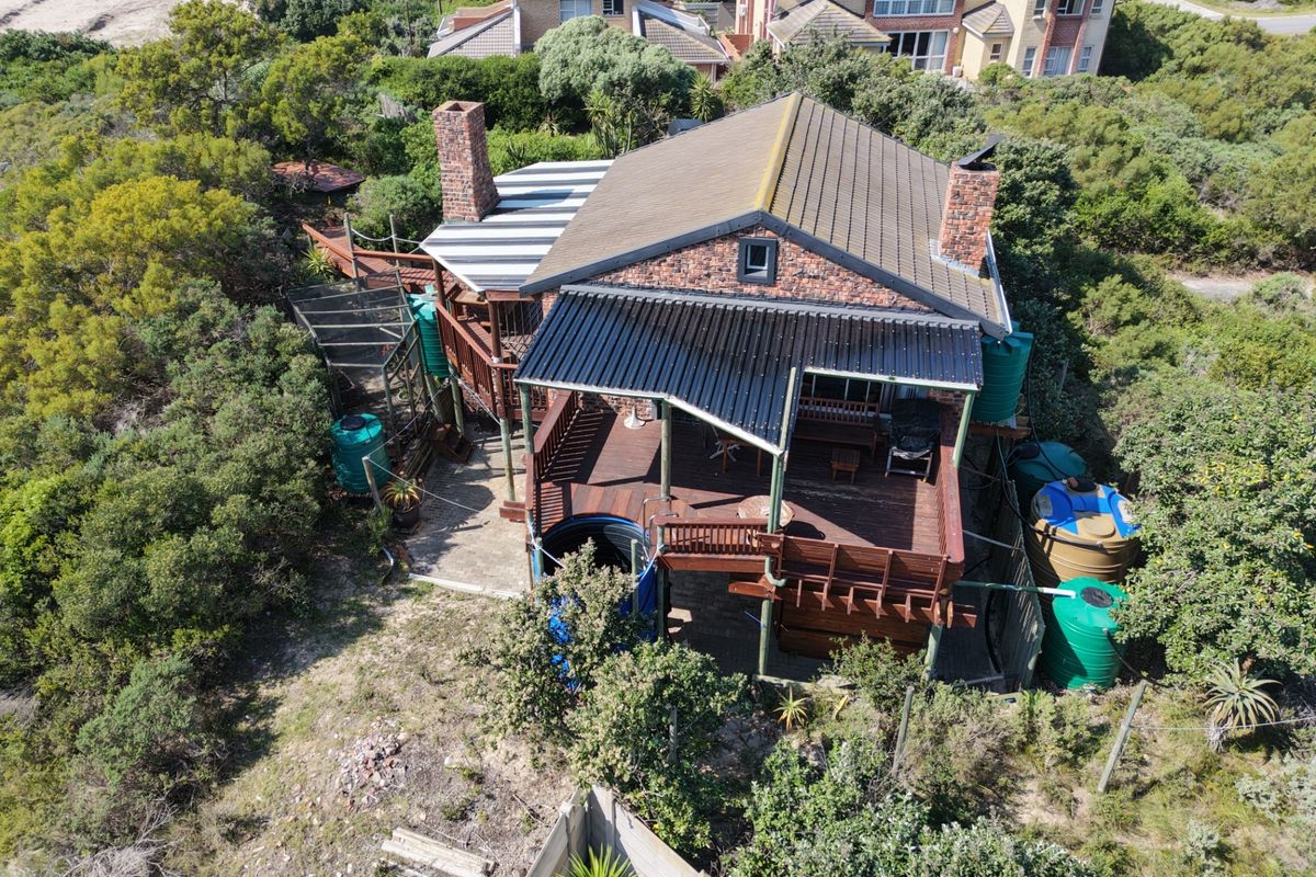 Aerial view of a detached house featuring a tiled roof, brick chimneys, extensive timber decking, and multiple water storage tanks set in a natural landscape.