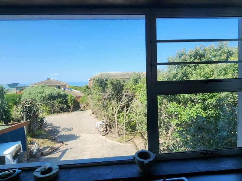 A view from an interior window looking out over a paved driveway, surrounding greenery, and distant coastal landscape.
