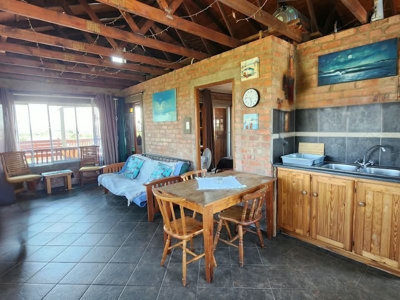 Open-plan living and kitchen area featuring exposed brick walls, timber beam ceilings, tiled floors, and functional built-in cabinetry with a stainless steel sink.