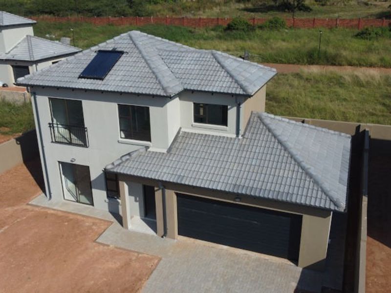 Aerial view of a modern double-storey residential property featuring a tiled roof, solar water heating system, double garage, and paved driveway.
