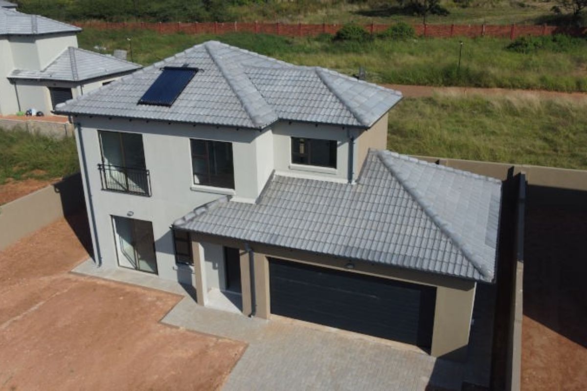 Aerial view of a modern double-storey residential property featuring a tiled roof, solar water heating system, double garage, and paved driveway.