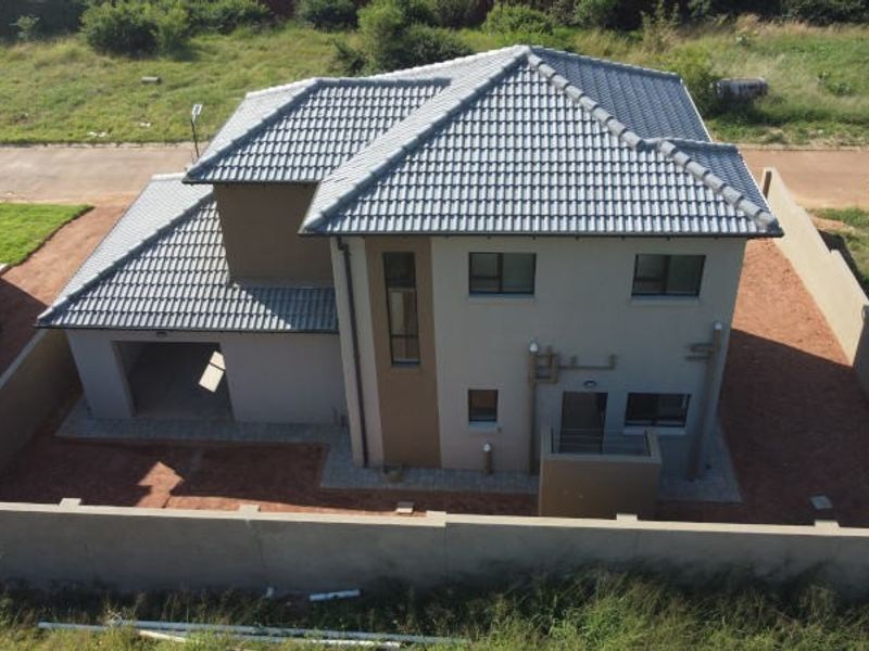 Aerial view of a modern two-story house featuring a tiled roof, attached garage, and a perimeter wall, set on an unlandscaped plot.