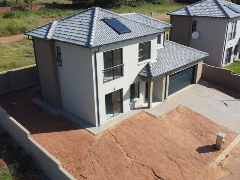 Aerial view of a modern two-story residential house featuring a tiled roof with solar heating, a paved driveway, and an enclosed perimeter wall.