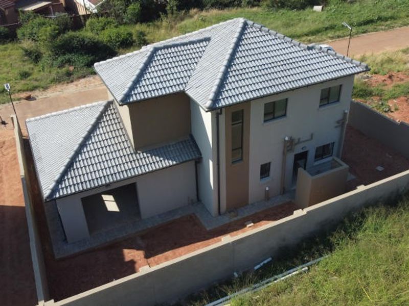Aerial view of a modern two-story house featuring a tiled roof, perimeter wall, and an integrated garage, set within an unfinished residential plot.