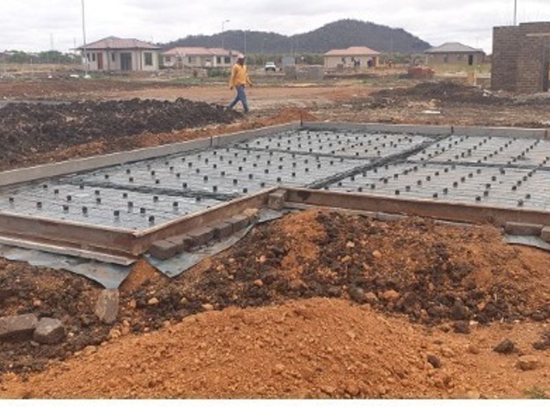 A construction site showing a prepared concrete foundation slab with steel reinforcement mesh and formwork in place for a new residential building.