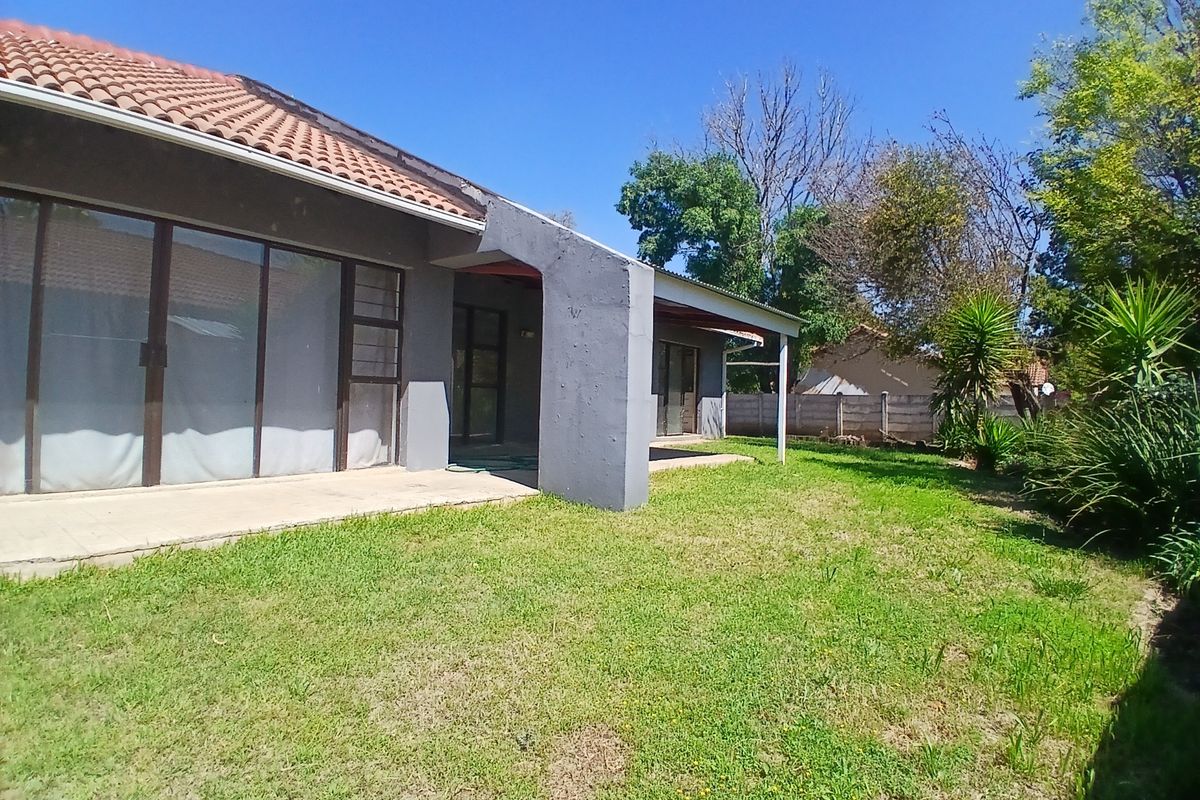 Rear view of the house featuring a concrete patio, sliding glass doors, and a spacious garden area with a perimeter wall.