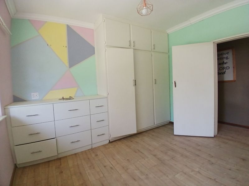 A bedroom featuring laminate flooring, built-in cupboards with overhead storage, and a decorative painted feature wall.