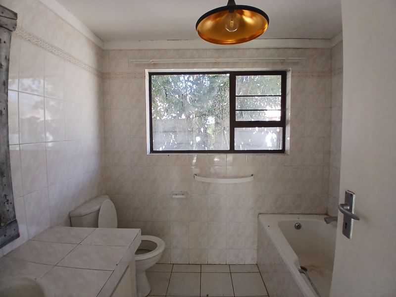 A dated bathroom featuring tiled walls and floors, a built-in vanity, a standard toilet, and a bathtub, offering potential for modernization.