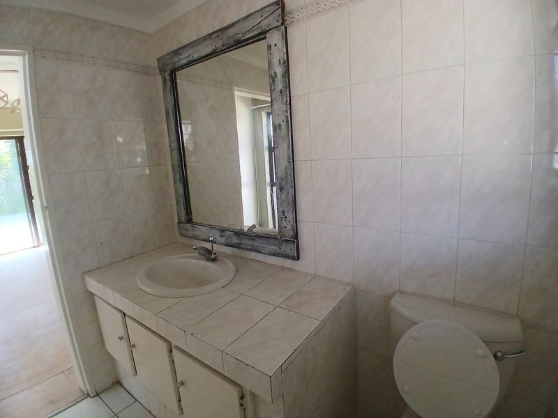 A functional bathroom featuring a tiled vanity with a drop-in sink, wall-mounted mirror, and standard toilet, finished with neutral wall tiles.