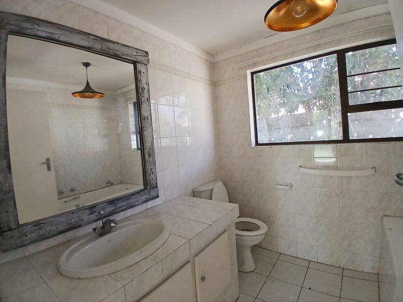 A dated bathroom featuring a tiled vanity with drop-in basin, toilet, and bathtub, finished with full-height wall tiling and tiled flooring.