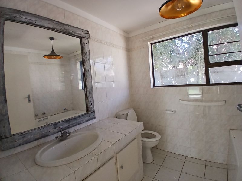 A functional bathroom featuring a tiled vanity with drop-in basin, toilet, bathtub, and full-wall tiling, offering a neutral base for potential modernization.
