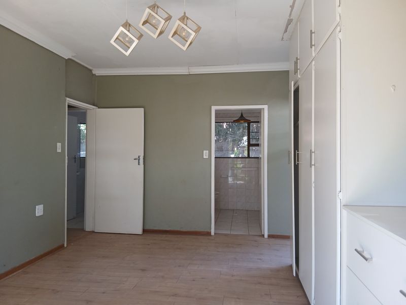A spacious, empty bedroom featuring light laminate flooring, built-in cupboards, and neutral wall tones, with an adjoining bathroom entrance.