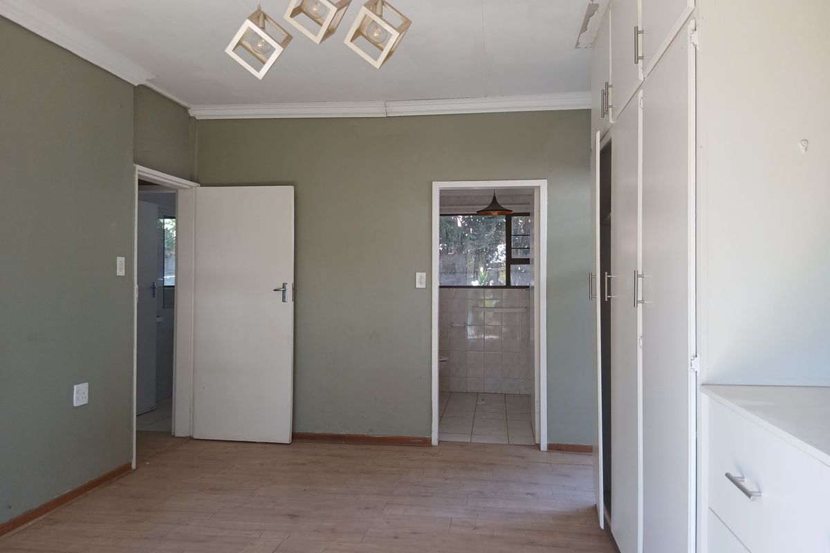 A spacious, empty bedroom featuring light laminate flooring, built-in cupboards, and neutral wall tones, with an adjoining bathroom entrance.