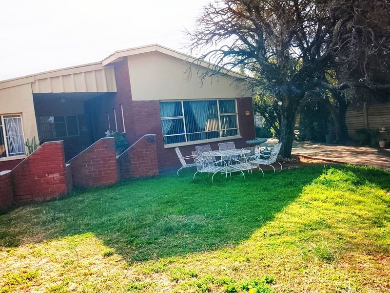 Rear view of the house featuring a brick facade, covered patio area, and established garden space.
