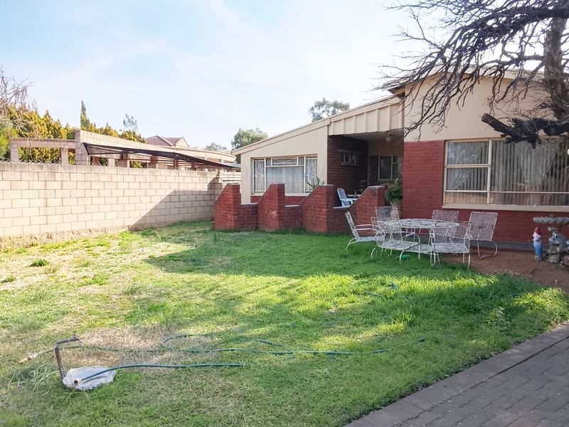 Rear view of the property featuring a brick facade, a covered patio area, and a private garden enclosed by a perimeter wall.