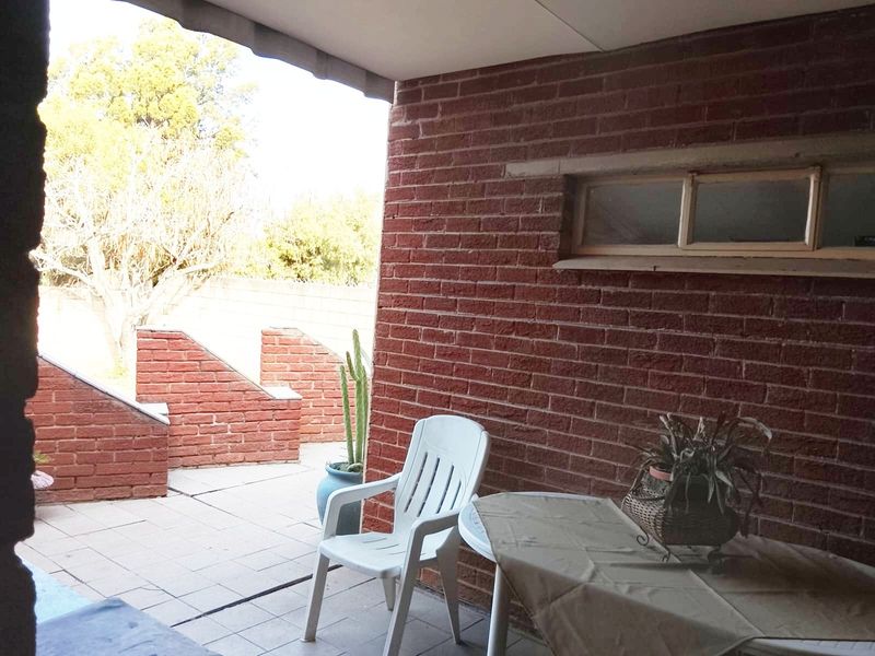 A covered outdoor patio area featuring exposed brick walls, tiled flooring, and a horizontal window, providing a functional space for outdoor relaxation.
