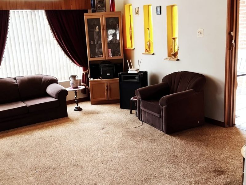 A living room featuring a timber-lined raked ceiling, recessed wall niches, and carpet flooring, offering a dated aesthetic ready for modernization.