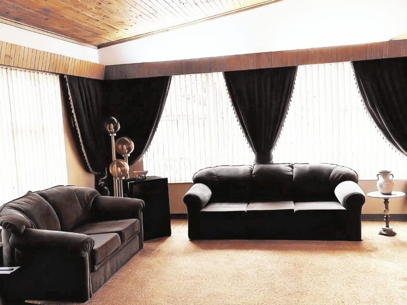 Spacious living room featuring a high vaulted timber-clad ceiling, large windows providing ample natural light, and carpeted flooring.