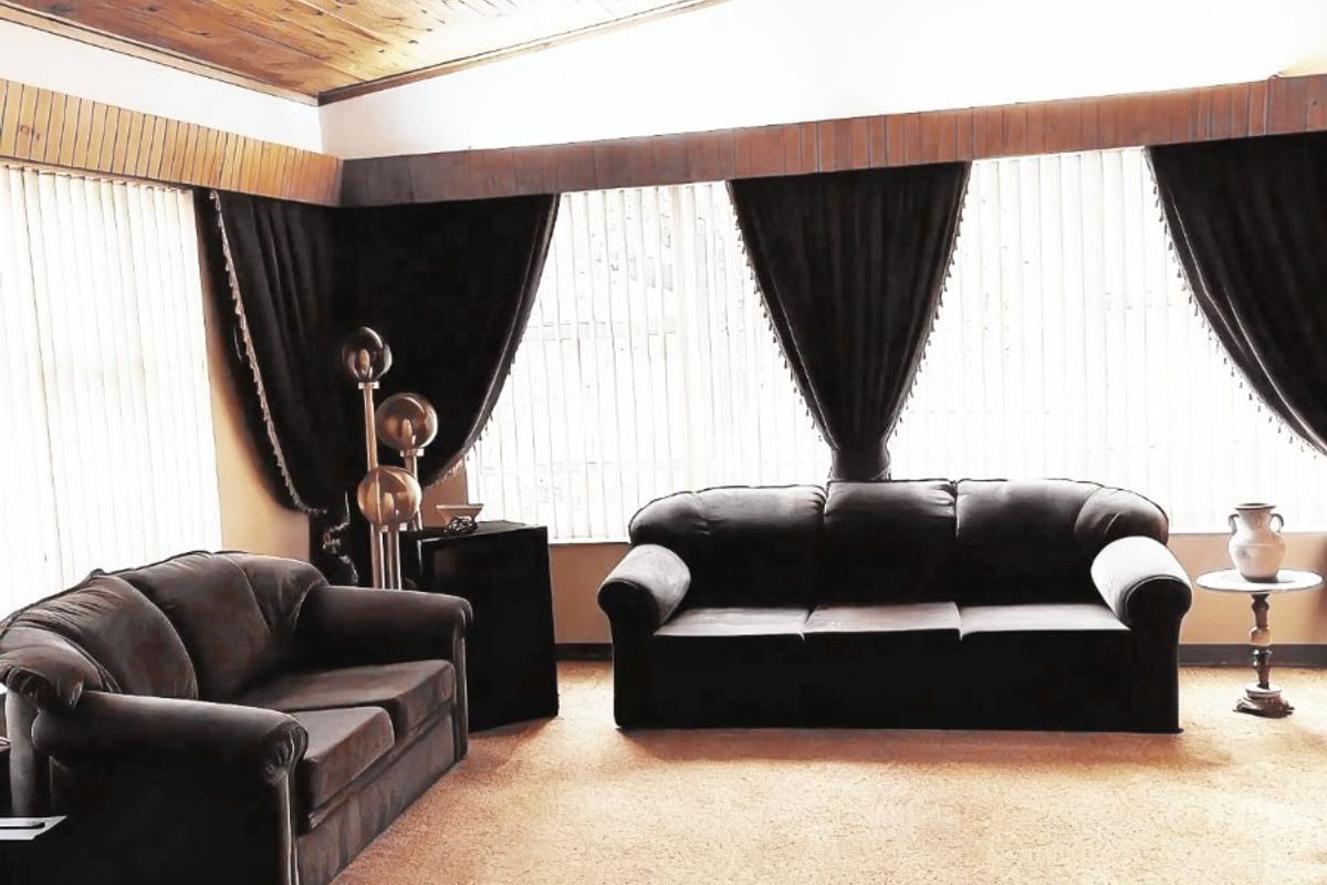 Spacious living room featuring a high vaulted timber-clad ceiling, large windows providing ample natural light, and carpeted flooring.