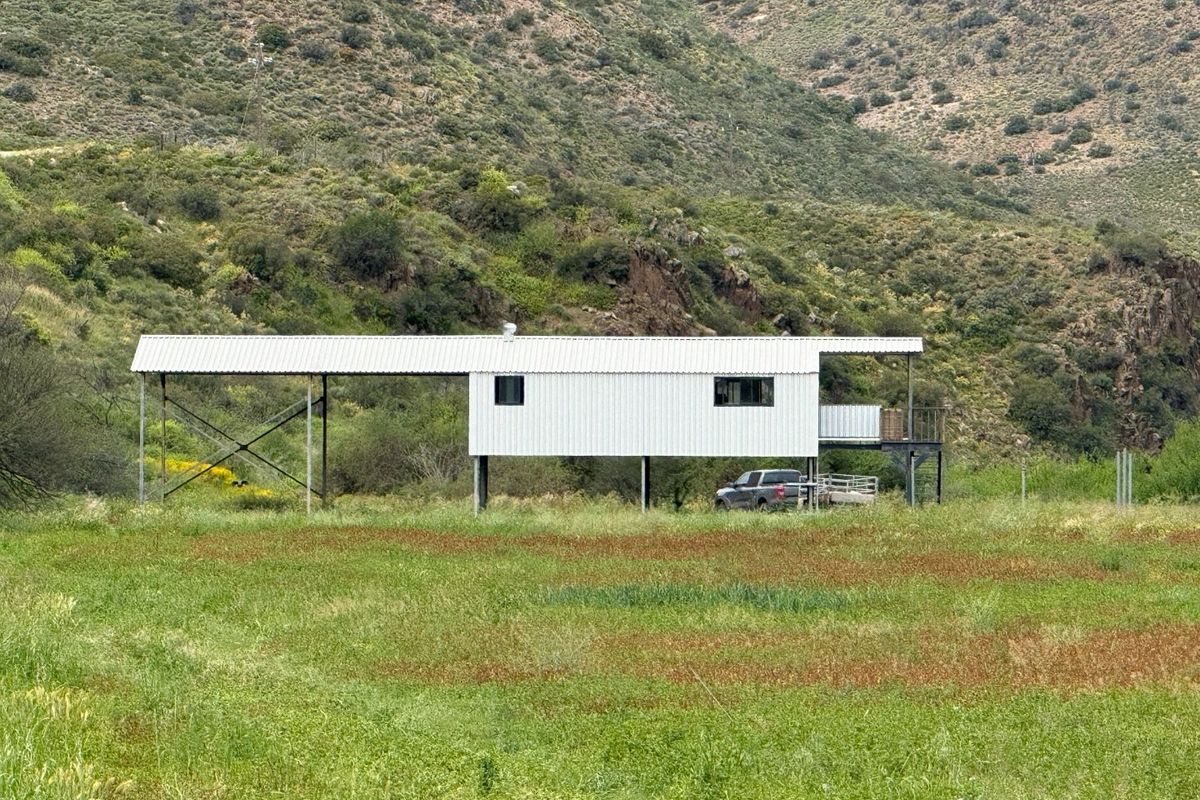 A modern elevated dwelling featuring corrugated metal cladding, a covered carport, and a balcony, set against a scenic mountainous landscape.