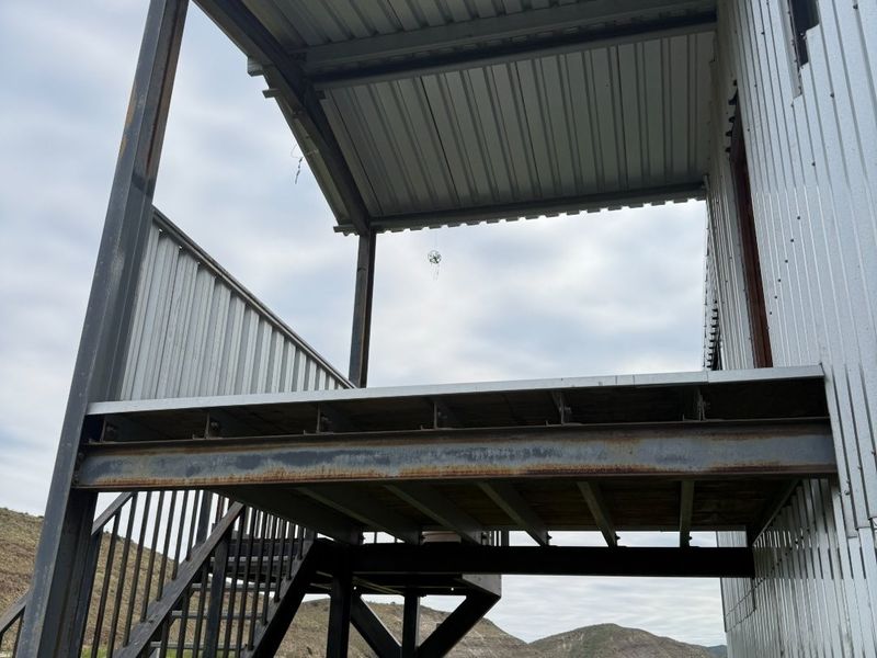 An elevated outdoor balcony featuring a corrugated metal roof and steel staircase, overlooking the surrounding landscape.