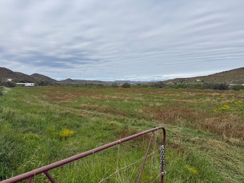 Expansive open field landscape with mountain views, featuring a metal farm gate in the foreground.