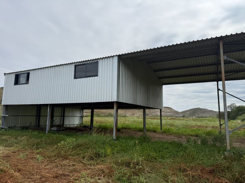 An elevated industrial-style structure featuring corrugated metal cladding and roofing, supported by steel columns, set within a rural landscape.