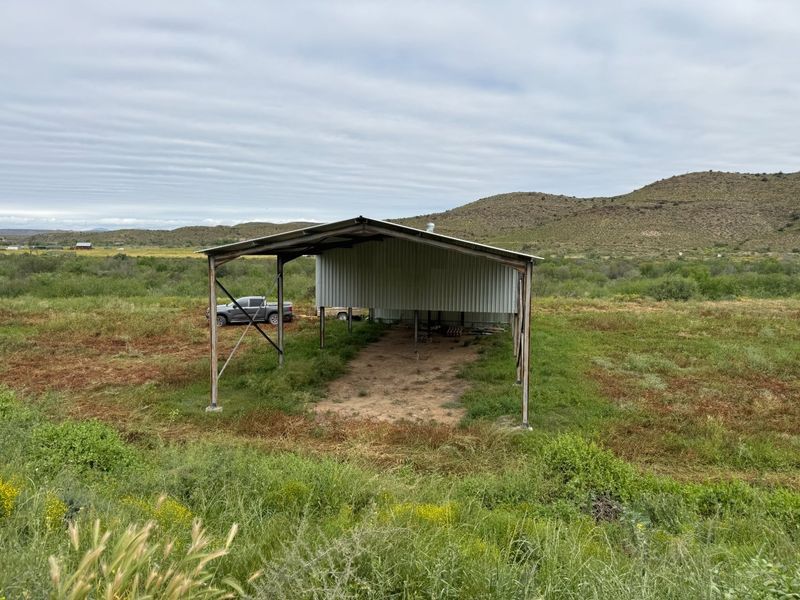 An open-sided metal utility structure or shed located on a rural small holding, suitable for storage or agricultural use.
