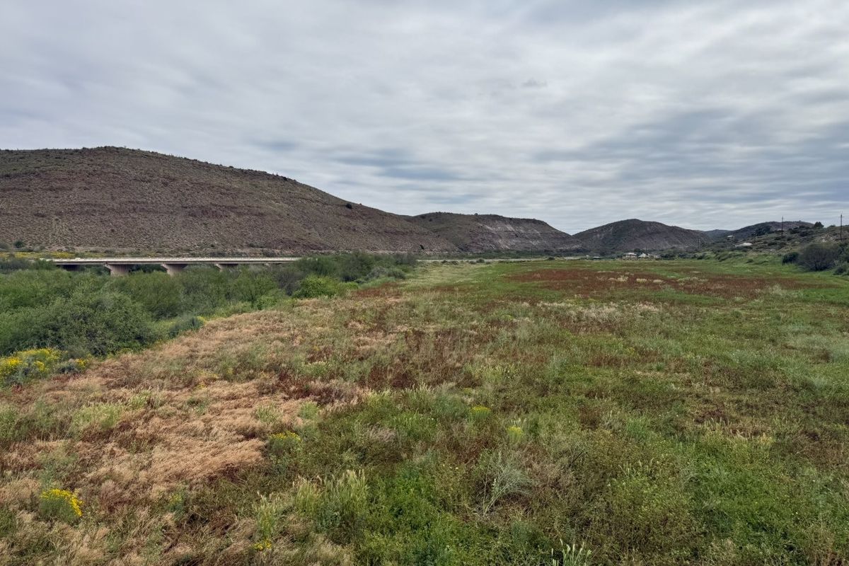 A scenic landscape view featuring rolling hills, natural vegetation, and a distant bridge structure.