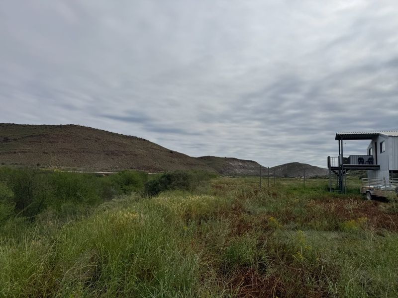 A scenic landscape view featuring rolling hills and natural vegetation with a glimpse of an elevated metal structure on the property.