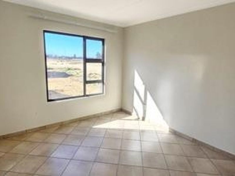 A bright, empty bedroom featuring neutral wall finishes, tiled flooring, and a large window providing natural light.