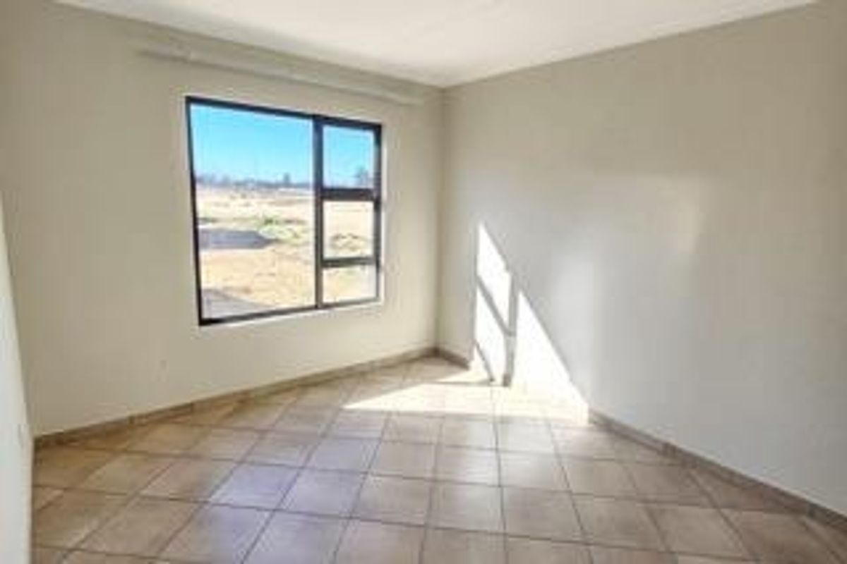 A bright, empty bedroom featuring neutral wall finishes, tiled flooring, and a large window providing natural light.