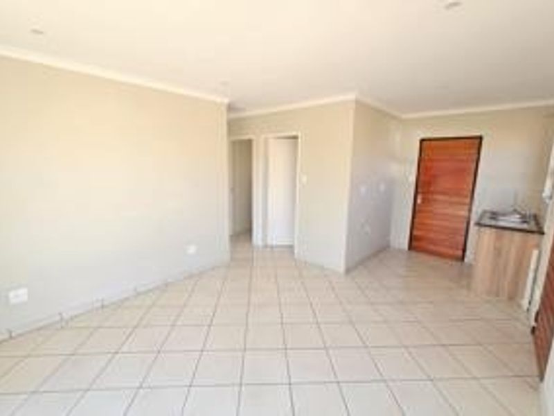 An open-plan living area featuring neutral tiled flooring, recessed lighting, and a small built-in kitchenette unit, presenting a clean and versatile space.