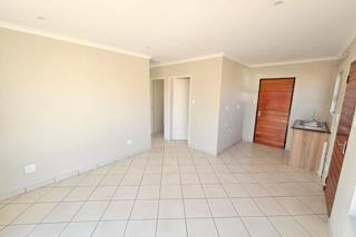 An open-plan living area featuring neutral tiled flooring, recessed lighting, and a small built-in kitchenette unit, presenting a clean and versatile space.