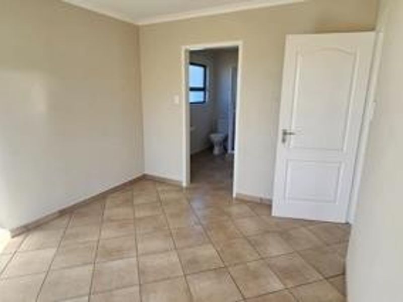 An empty bedroom featuring neutral walls, tiled flooring, and an adjoining en-suite bathroom.