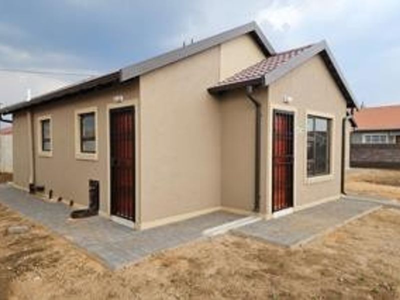 A well-maintained rear exterior view of a modern house featuring a tiled roof, paved walkways, and secure entrance doors.