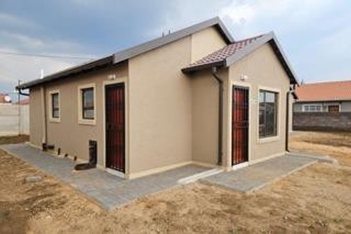 A well-maintained rear exterior view of a modern house featuring a tiled roof, paved walkways, and secure entrance doors.