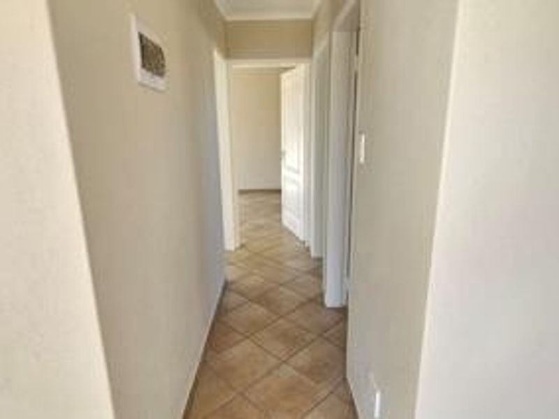 A clean, neutral hallway featuring tiled flooring and access to multiple rooms, providing a functional transition space within the home.