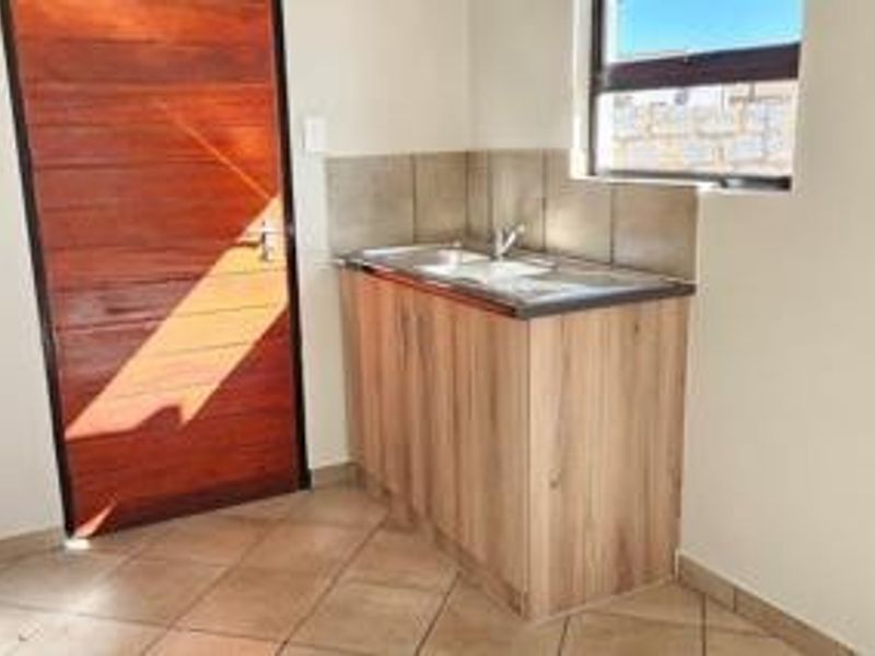 A functional scullery or utility area featuring a stainless steel sink, wooden cabinetry, tiled splashback, and tiled flooring with a timber door.