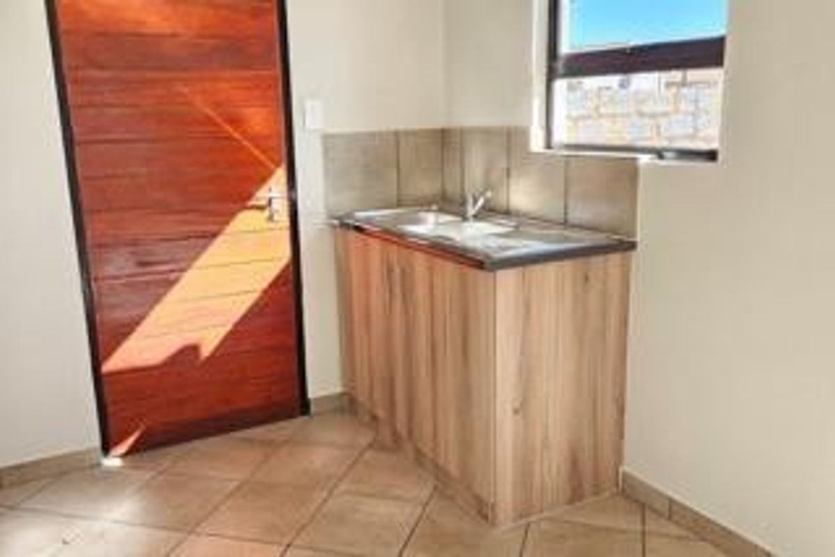 A functional scullery or utility area featuring a stainless steel sink, wooden cabinetry, tiled splashback, and tiled flooring with a timber door.