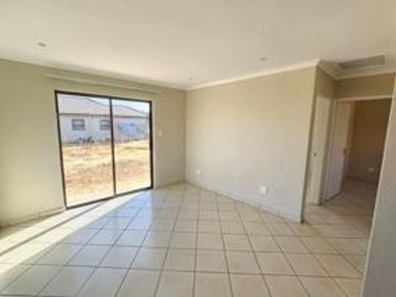 A bright, empty living area featuring neutral tiled flooring, recessed lighting, and a large sliding glass door providing access to the exterior.