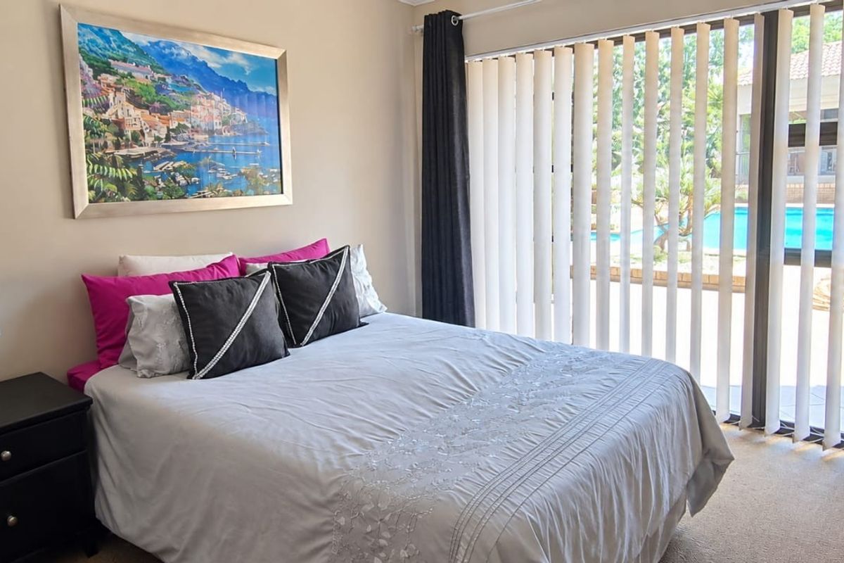 A well-maintained bedroom featuring carpeted flooring and a large sliding glass door with vertical blinds, providing direct access to the pool area.