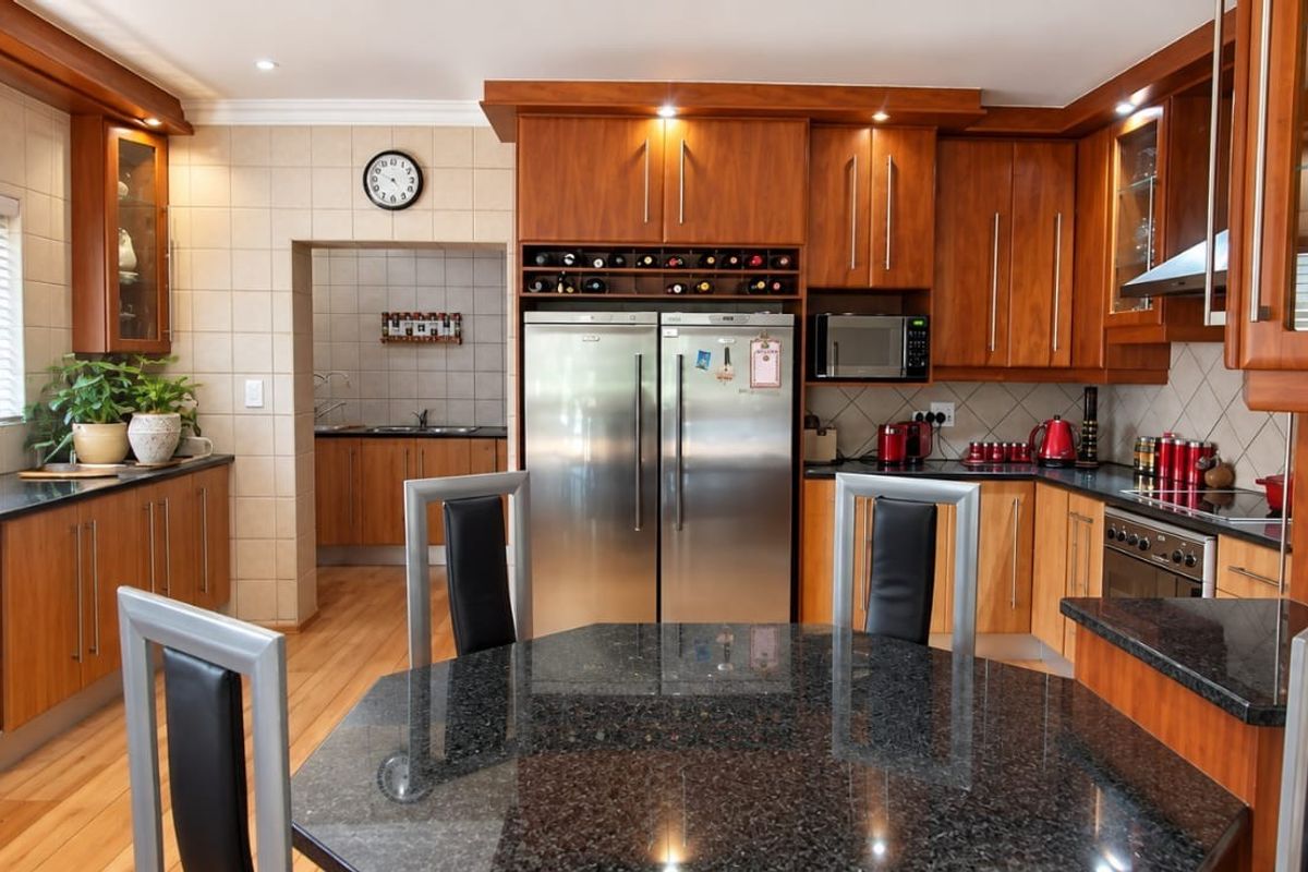 Spacious kitchen featuring warm wooden cabinetry, granite countertops, integrated appliances, and a separate scullery area, offering a functional and well-maintained cooking space.
