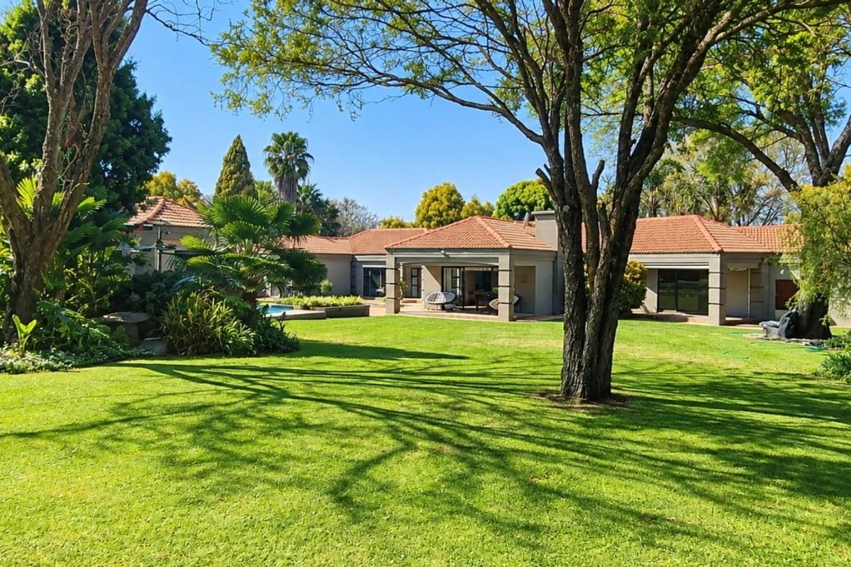 Spacious rear garden featuring a well-maintained lawn, mature trees, a swimming pool, and a covered patio area attached to the main residence.