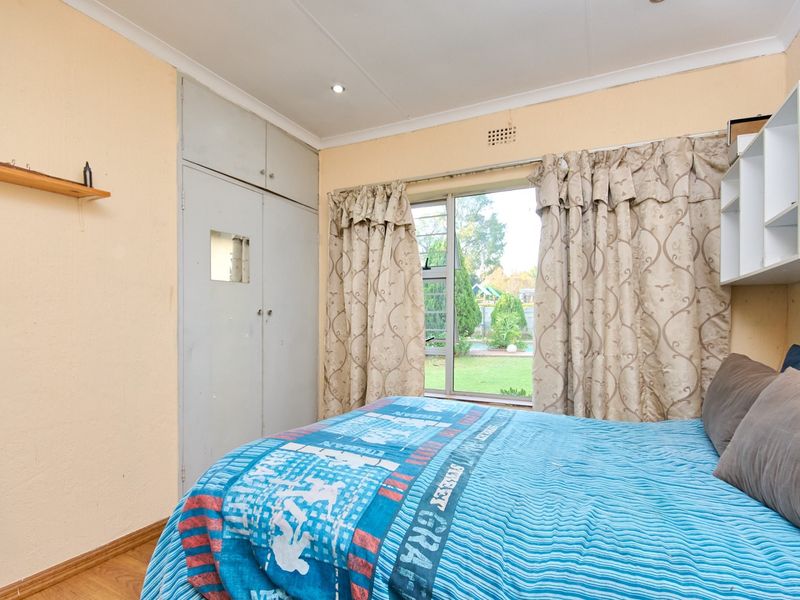 A bedroom featuring built-in cupboards, laminate flooring, and a window overlooking the garden, offering a functional space with potential for cosmetic updates.