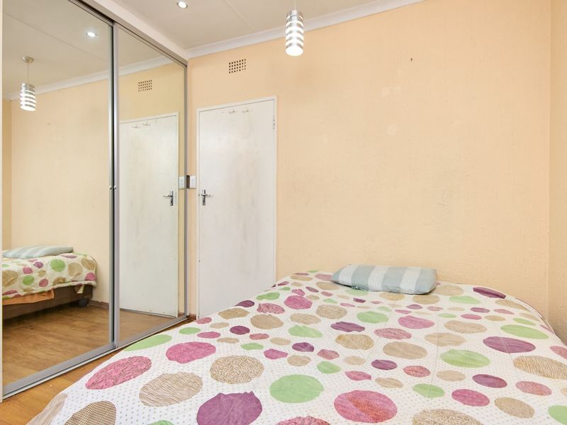 A bedroom featuring laminate flooring, a large mirrored sliding wardrobe, and neutral wall finishes with integrated lighting.