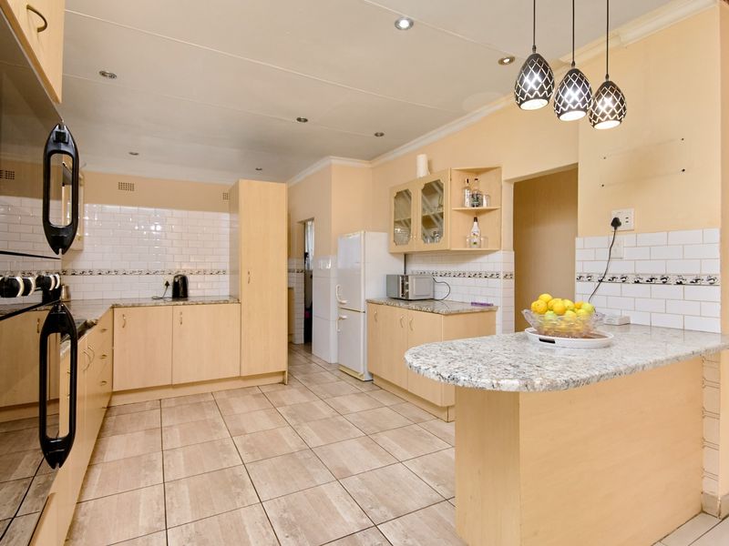 A functional kitchen featuring light wood cabinetry, granite countertops, subway tile backsplash, and a breakfast bar with modern pendant lighting.
