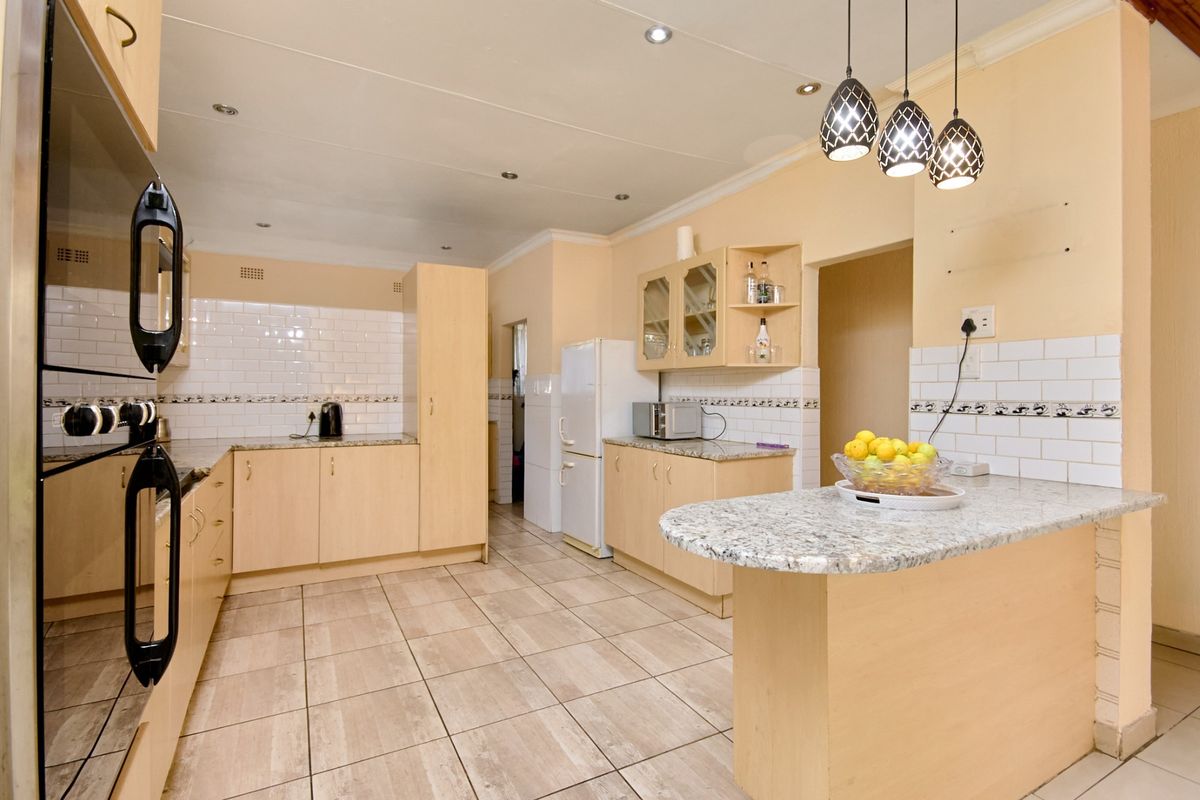 A functional kitchen featuring light wood cabinetry, granite countertops, subway tile backsplash, and a breakfast bar with modern pendant lighting.