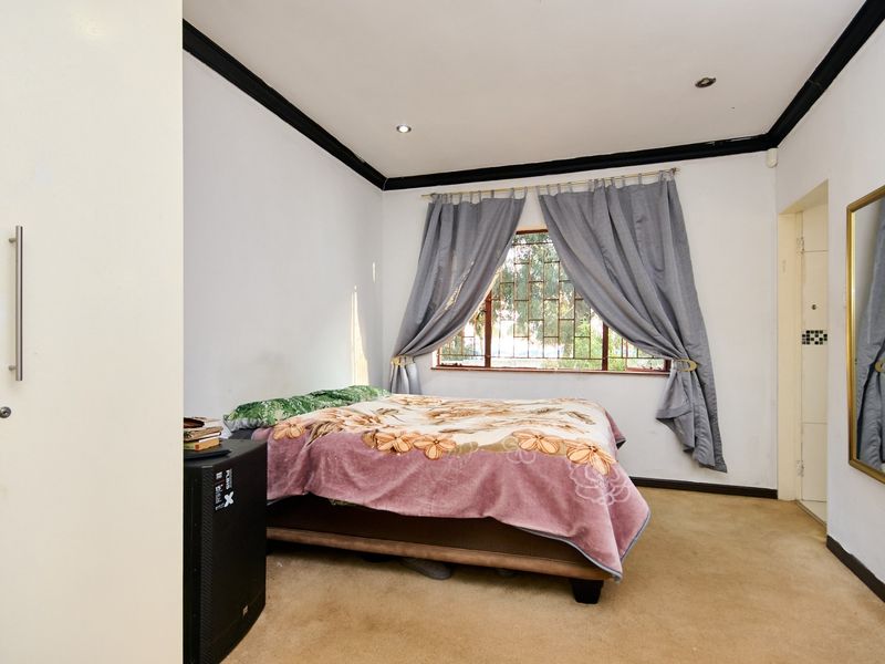 A bedroom featuring built-in wardrobes, recessed downlighting, and security bars on the window. The room includes carpet flooring and decorative cornice detailing.